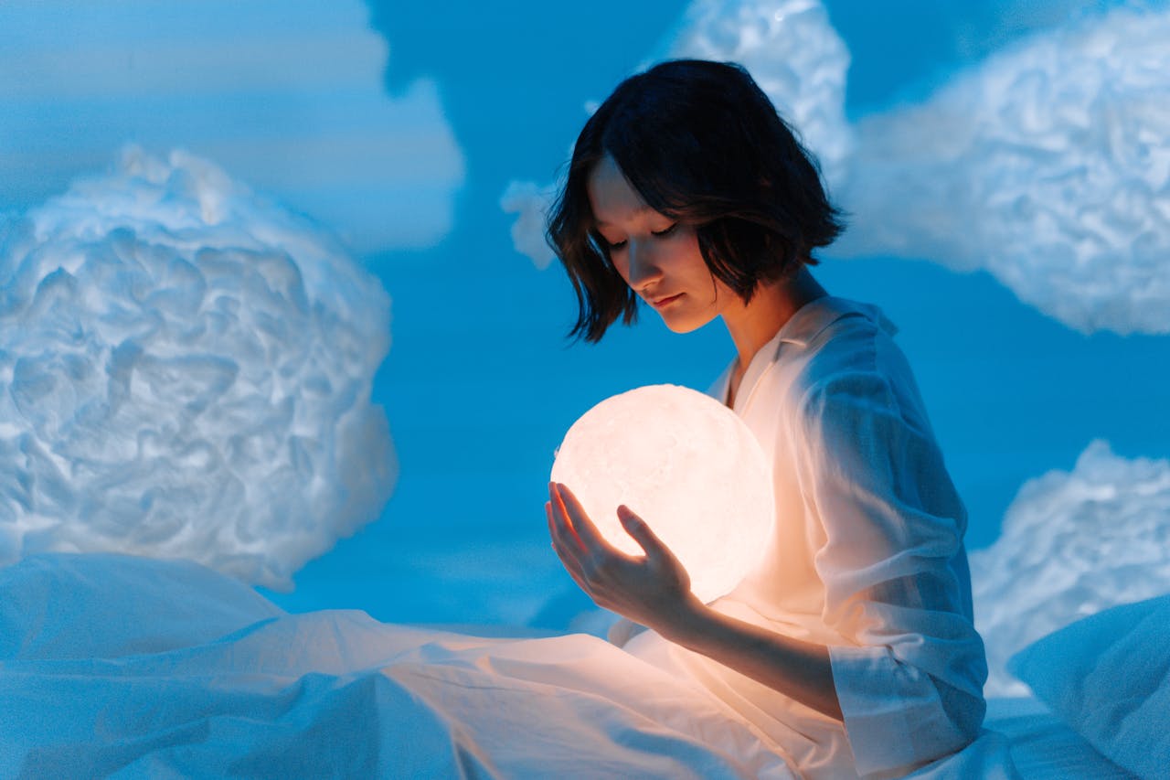 A woman in a dream-like setting holding a glowing sphere surrounded by cloud-like formations.